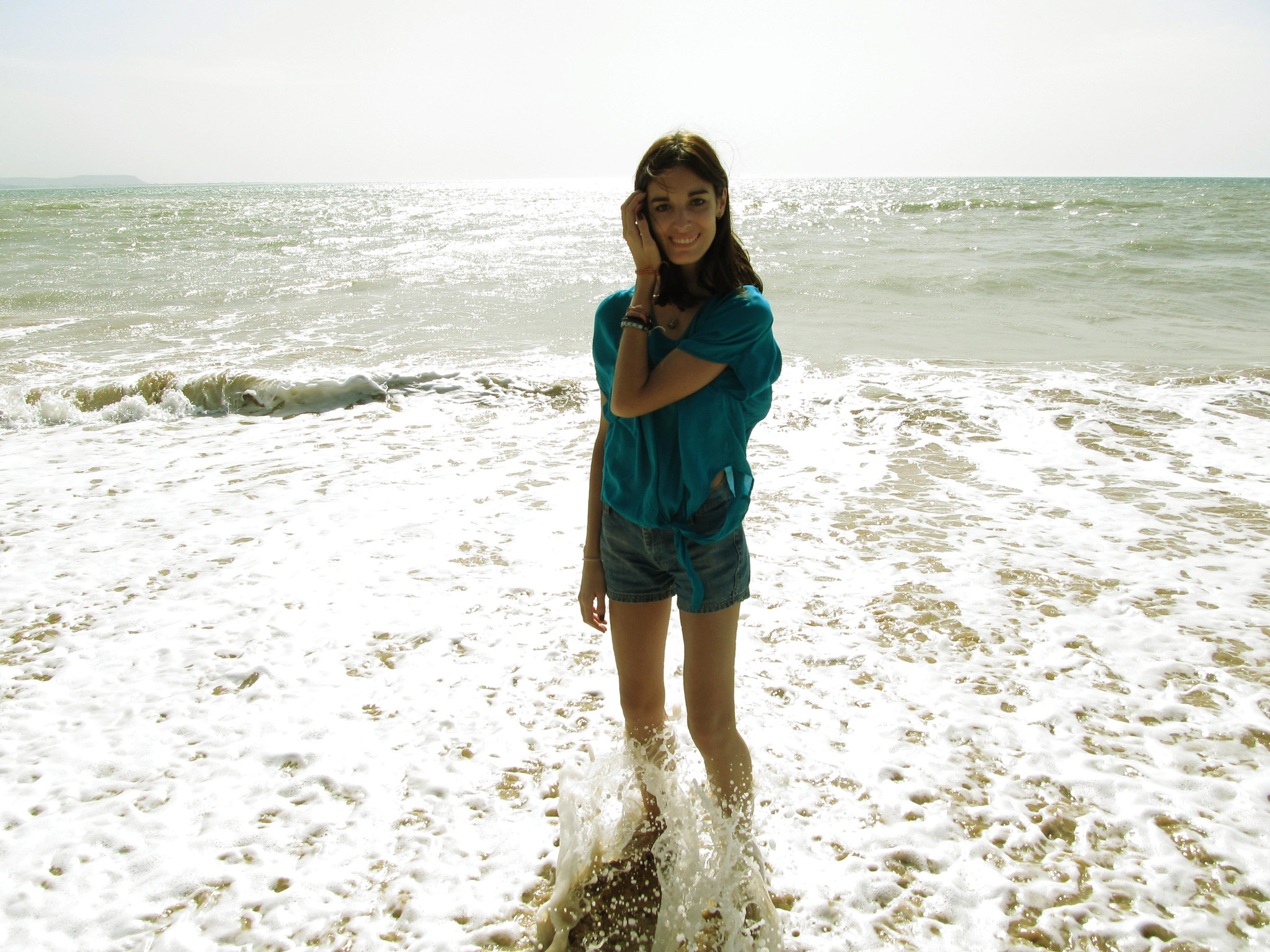 A young woman smiling while standing in water at a beach | Source: Flickr