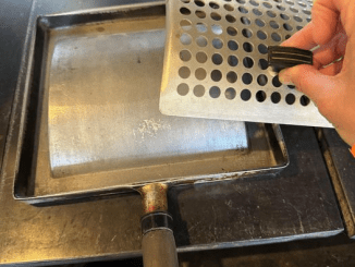 A 6-inch square kitchen implement, made from metal with a possibly bone handle, was located on a stove in an early 1900s American home.